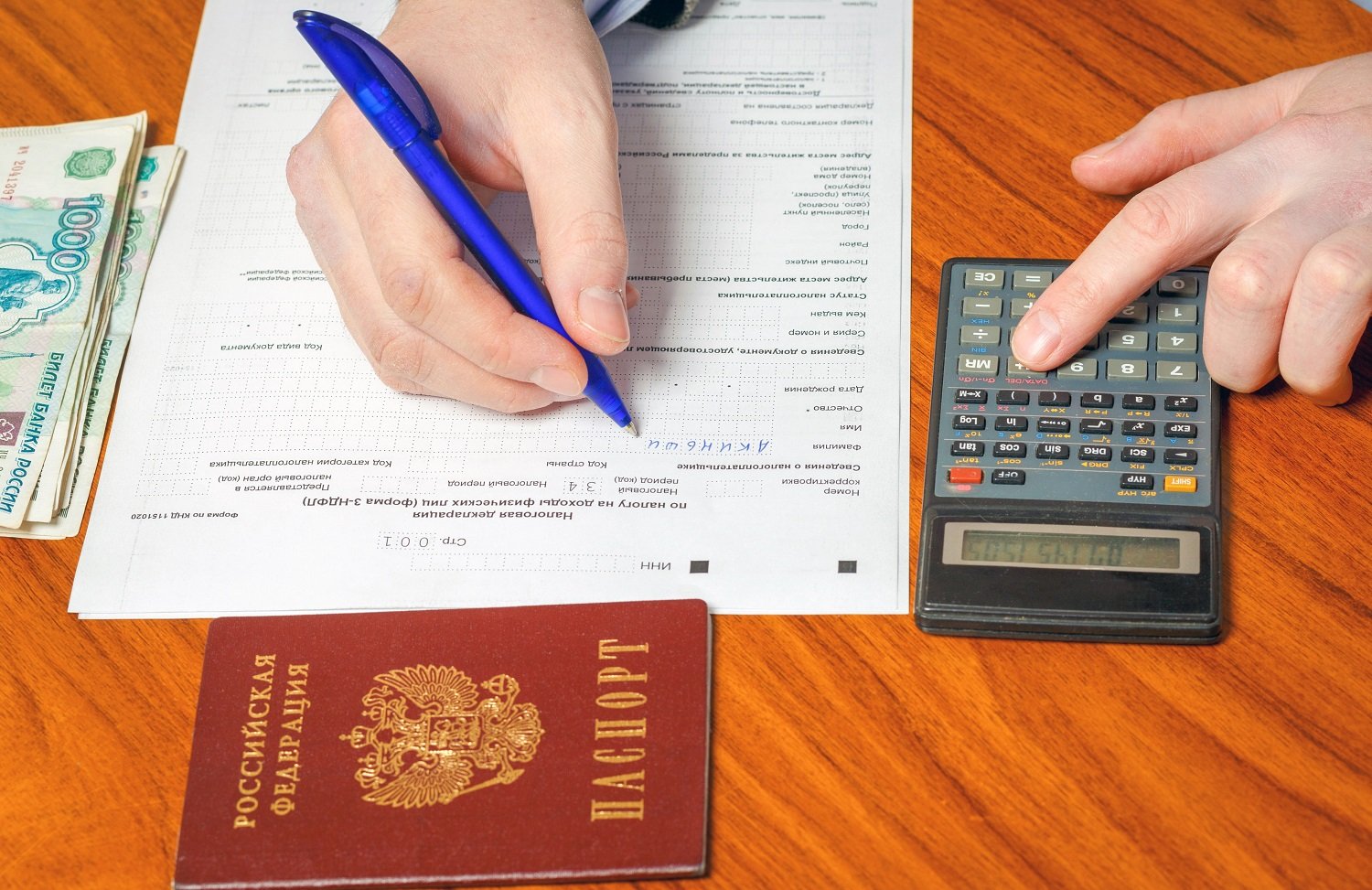 一个人拿着笔填写俄罗斯纳税申报表。 表格旁边是一小堆俄罗斯钞票和一个计算器。 该人按下计算器上的一个键。